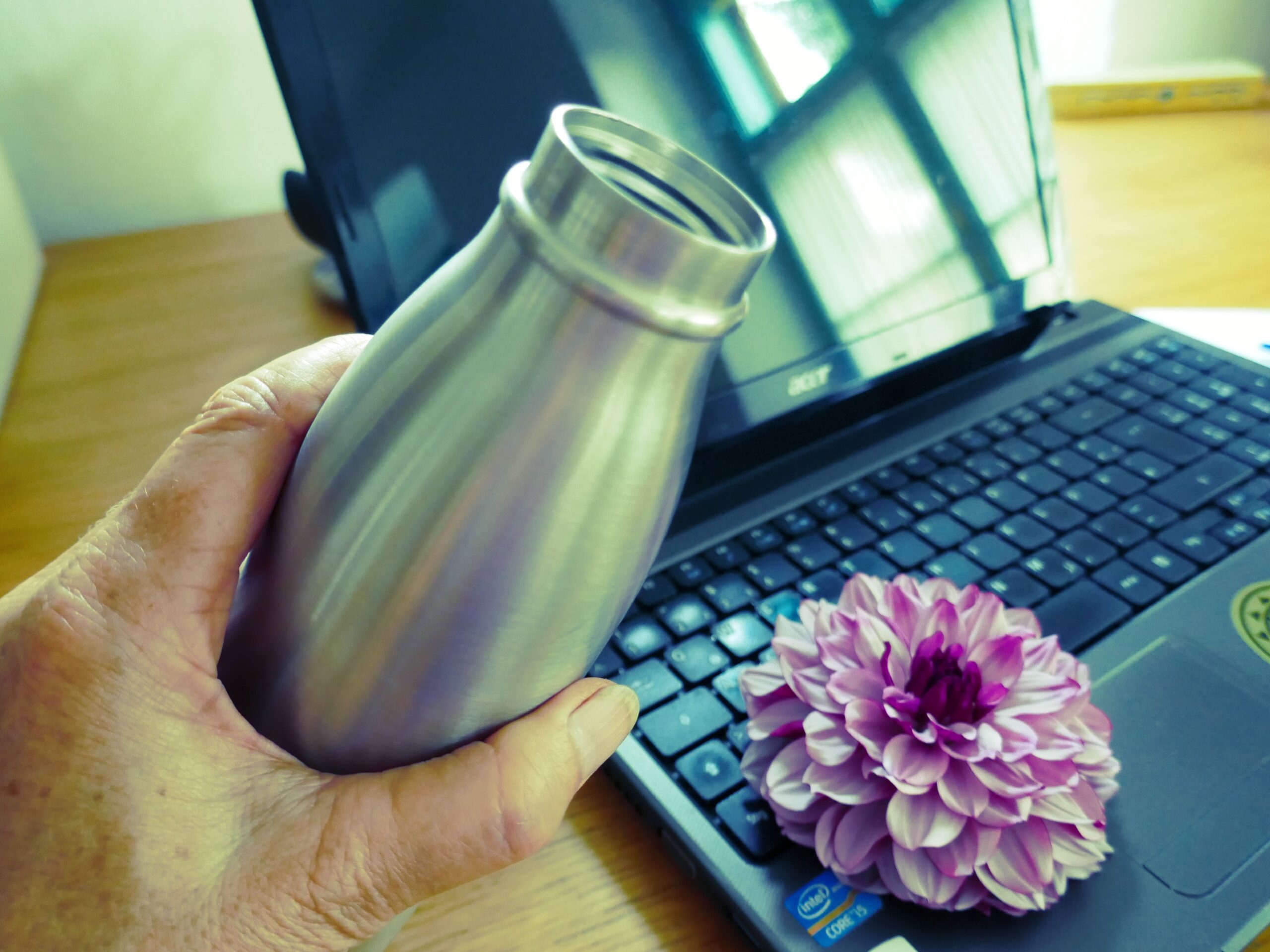 eine Hand hält eine Trinkflasche, dahinter sieht man ein Notebook mit einer Lotusblüte darauf